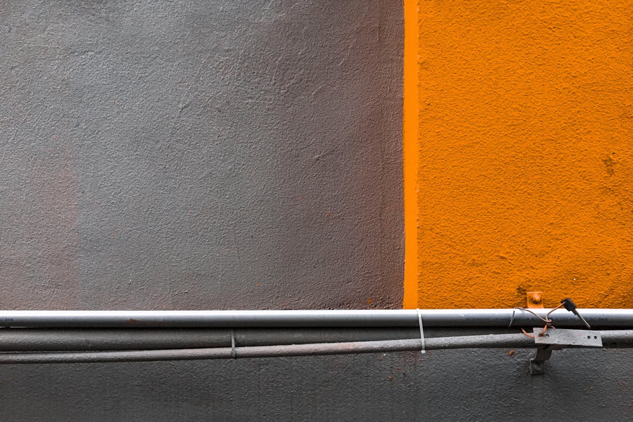 Abstract urban background featuring grey and orange textured concrete wall with pipelines.